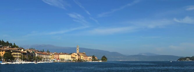 Trip Reiseideen beliebte Urlaubsziele am Gardasee -  Mit einer Fläche von 370 km² ist der Gardasee der größte See Italiens. Es liegt am Fuße der Alpen und erstreckt sich über drei Staaten: Lombardei, Venetien und Trentino. Die maximale Tiefe des Sees beträgt 346 m, er hat eine längliche Form und sein nördliches Ende ist sehr schmal. Dort ist der See von den Bergen der Gruppo di Baldo umgeben. Du trittst aus deinem gemütlichen Hotelzimmer und es begrüßt dich die warme italienische Sonne. Du blickst auf den atemberaubenden Gardasee, der in zahlreichen Blautönen schimmert - von tiefem Dunkelblau bis zu funkelndem Türkis. Majestätische Berge umgeben dich, während die Brise sanft deine Haut streichelt und der Duft von blühenden Zitronenbäumen deine Nase kitzelt. Du schlenderst die malerischen, engen Gassen entlang, vorbei an farbenfrohen, blumengeschmückten Häusern. Vereinzelt unterbricht das fröhliche Lachen der Einheimischen die friedvolle Stille. Du fühlst dich wie in einem Traum, der nicht enden will. Jeder Schritt führt dich zu neuen Entdeckungen und Abenteuern. Du probierst die köstliche italienische Küche mit ihren frischen Zutaten und verführerischen Aromen. Die Sonne geht langsam unter und taucht den Himmel in ein leuchtendes Orange-rot - ein spektakulärer Anblick.